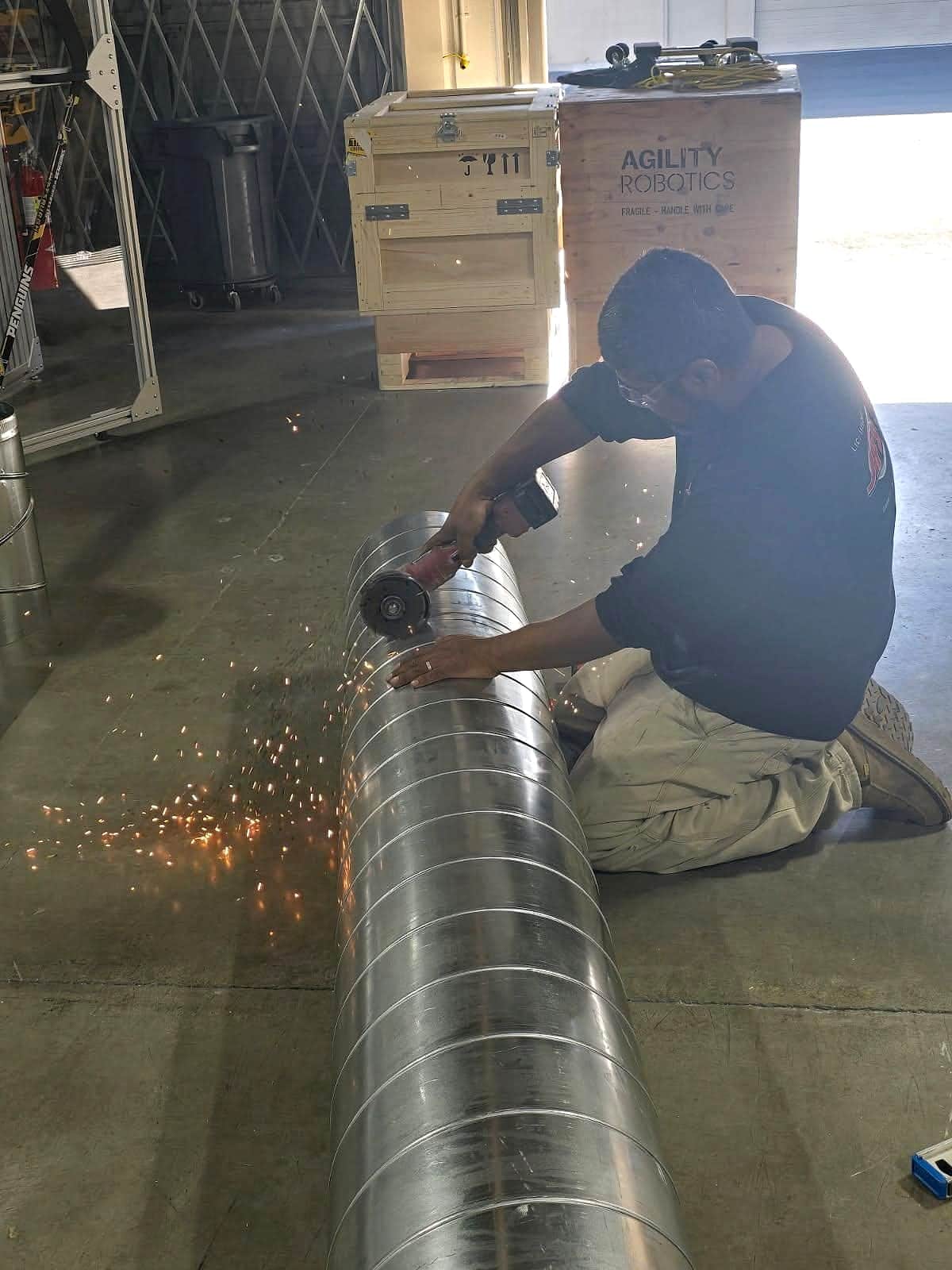 Technician cutting spiral duct with an angle grinder, sparks flying