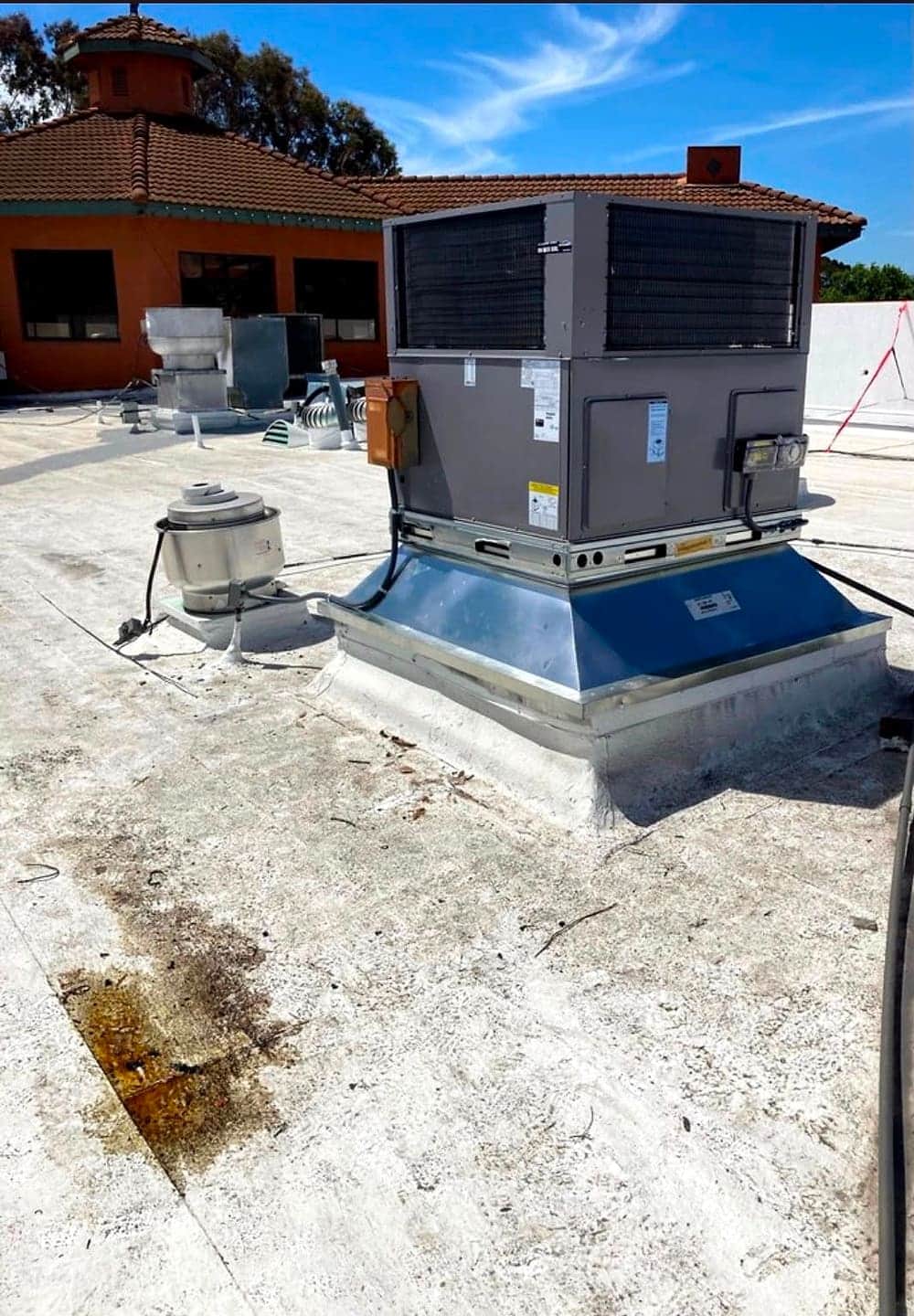 New packaged HVAC unit on a rooftop curb at a tile-roofed commercial building
